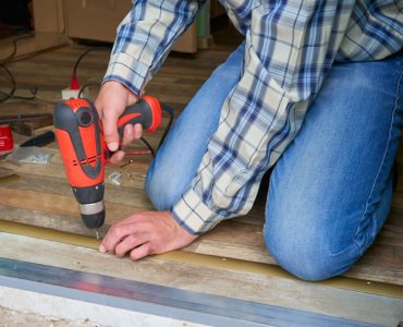 Un homme installe un seuil de plancher à l'aide de sa perceuse