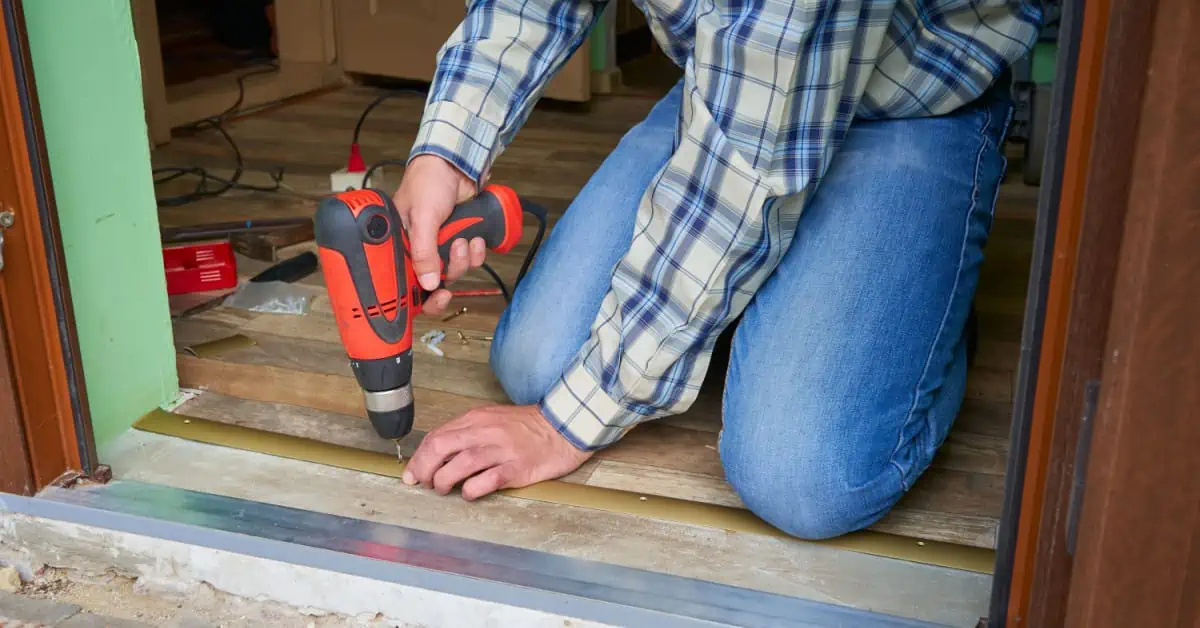 Un homme installe un seuil de plancher à l'aide de sa perceuse