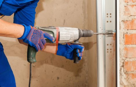 Un homme en combinaison bleu perce un trou au mur à l’aide d’une perceuse électrique