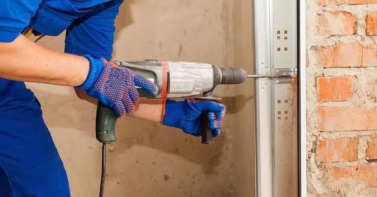 Un homme en combinaison bleu perce un trou au mur à l’aide d’une perceuse électrique