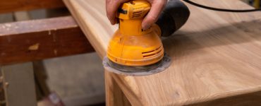 Zoom sur la main d’un homme utilisant une ponceuse orbitale pour poncer une table en bois