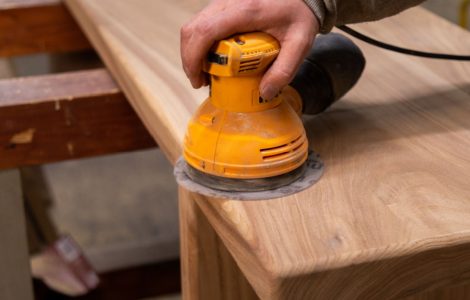 Zoom sur la main d’un homme utilisant une ponceuse orbitale pour poncer une table en bois