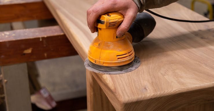 Zoom sur la main d’un homme utilisant une ponceuse orbitale pour poncer une table en bois