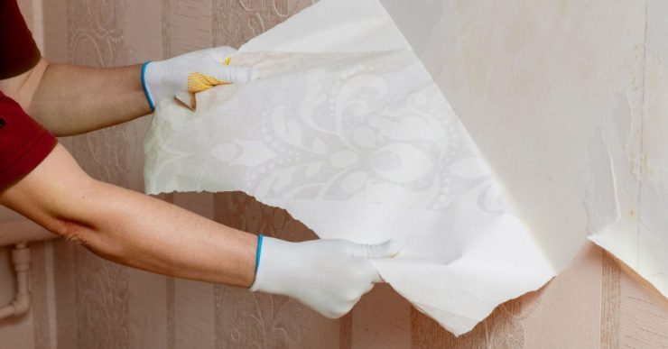 Un homme en gants blancs en train de décoller le papier peint du mur