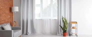 Salon spacieux avec un canapé gris et des rideaux clairs sur la fenêtre