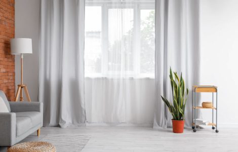 Salon spacieux avec un canapé gris et des rideaux clairs sur la fenêtre