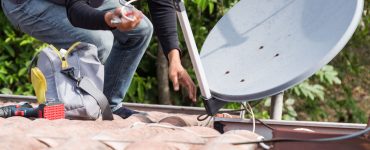 Un homme installe uen antenne parabolique sur le toit