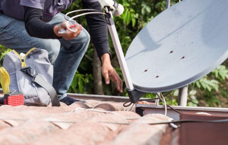 Un homme installe uen antenne parabolique sur le toit
