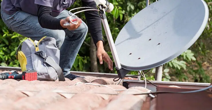 Un homme installe uen antenne parabolique sur le toit