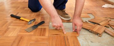 Un homme retire le vieux parquet en bois à l'aide d'un marteau jaune et d'un outil de raclage