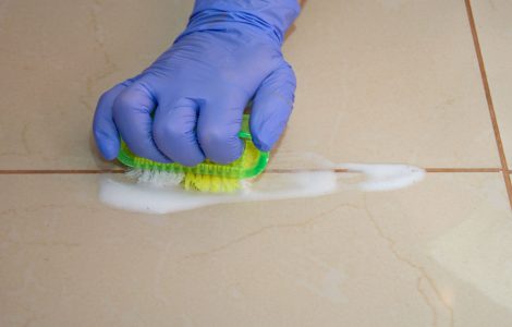 Zoom sur une main en gant bleu en train de nettoyer le carrelage