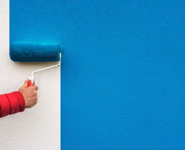 Focus sur la main d’une personne tenant un rouleau de peinture et peignant un mur en bleu