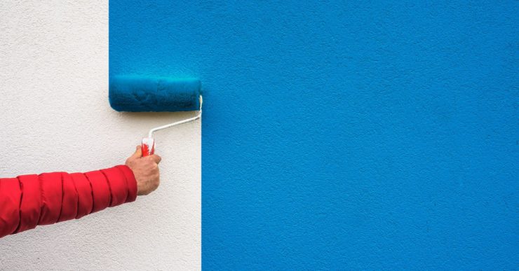 Focus sur la main d’une personne tenant un rouleau de peinture et peignant un mur en bleu
