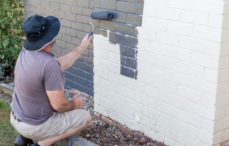 Un homme avec son rouleau peint un mur en briques en blanc