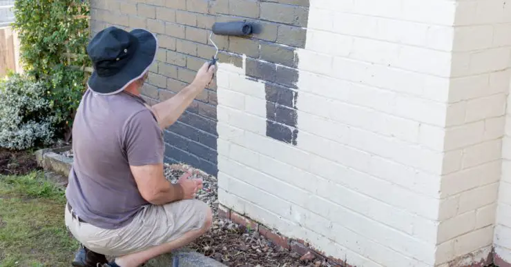 Un homme avec son rouleau peint un mur en briques en blanc