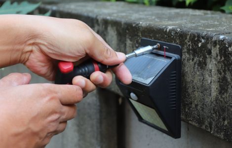 Un homme installe un projecteur solaire avec détecteur de mouvement sur un mur en béton