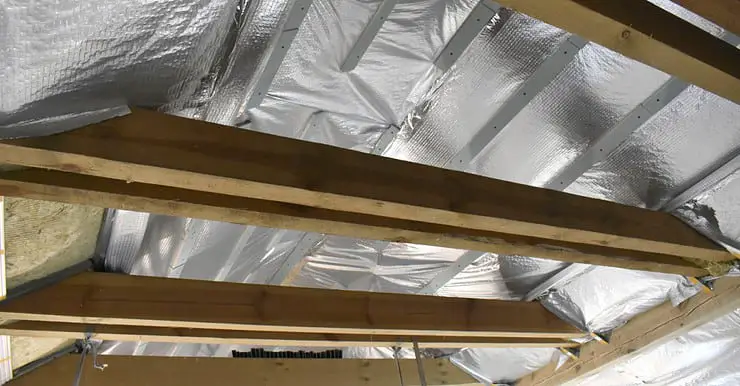 Isolation du toit par l'intérieur, vue sur les poutres en bois et le film d'isolation thermique