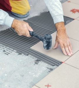 Un homme posant du carrelage tape le carreau avec un maillet