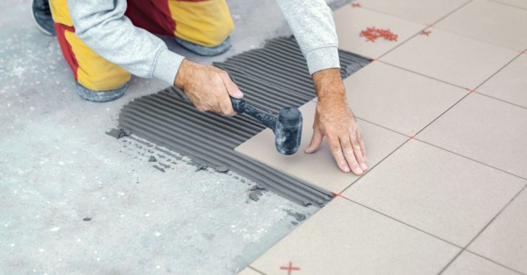 Un homme posant du carrelage tape le carreau avec un maillet