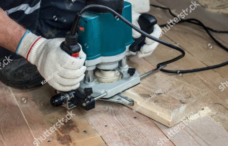 Zoom sur les mains d’un homme utilisant un rouleur électrique pour couper une planche en bois