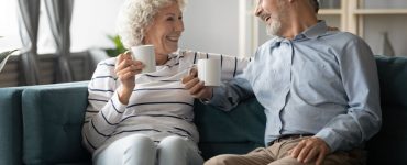 Couple mature souriant assis dans un canapé bleu et tenant des tasses blanches