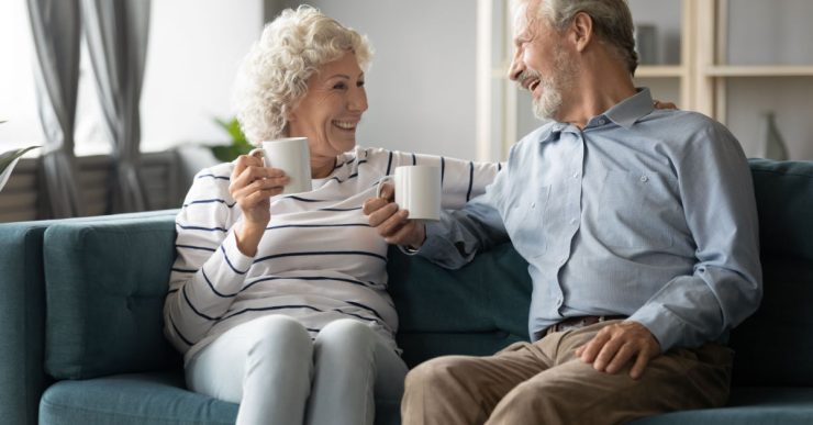 Couple mature souriant assis dans un canapé bleu et tenant des tasses blanches