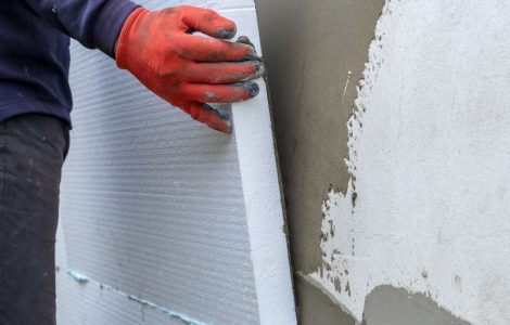 Un homme en gants rouges installant des feuilles d'isolation en polystyrène sur le mur de façade