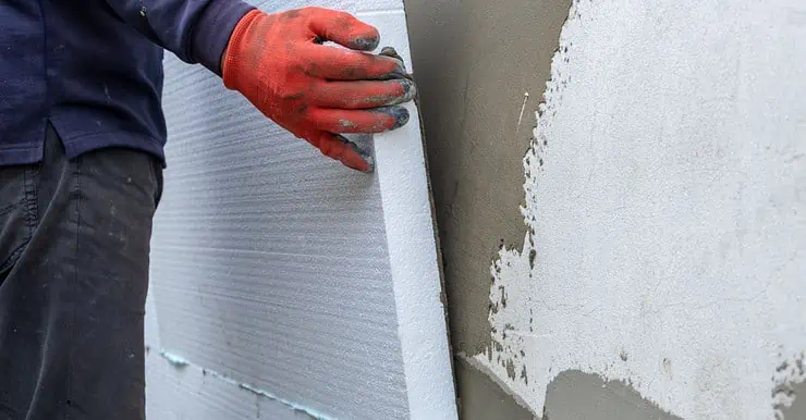 Un homme en gants rouges installant des feuilles d'isolation en polystyrène sur le mur de façade