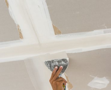 Zoom sur la main d'un homme en train de faire les joints de plâtre sur un plafond