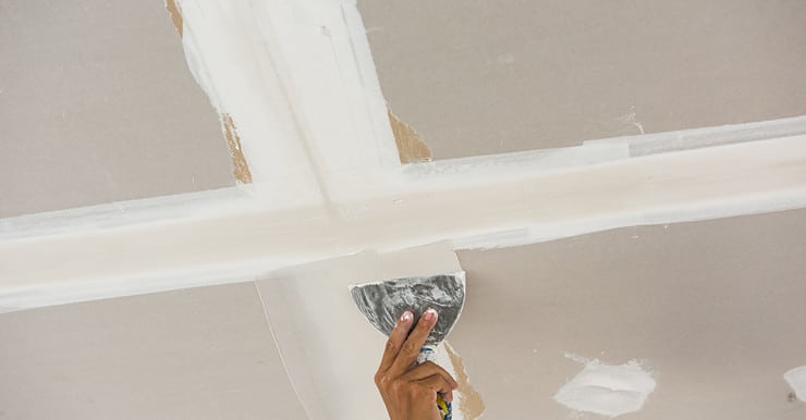 Zoom sur la main d'un homme en train de faire les joints de plâtre sur un plafond