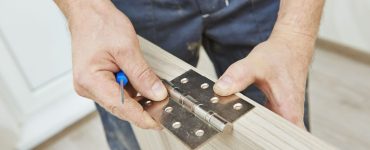 Gros plan sur les mains d’un homme installant les charnières d’une porte en bois