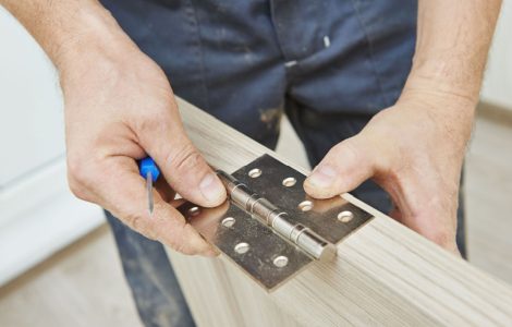 Gros plan sur les mains d’un homme installant les charnières d’une porte en bois