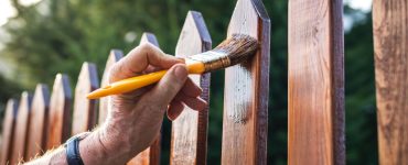 Zoom sur la main d'un homme appliquant un vernis sur une clôture en bois