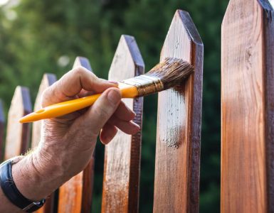 Zoom sur la main d'un homme appliquant un vernis sur une clôture en bois