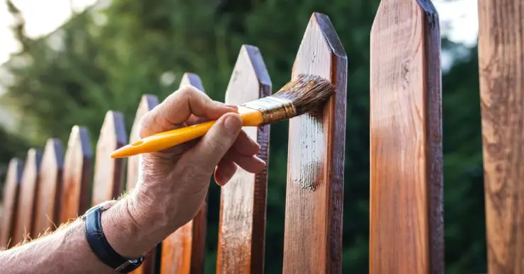 Zoom sur la main d'un homme appliquant un vernis sur une clôture en bois