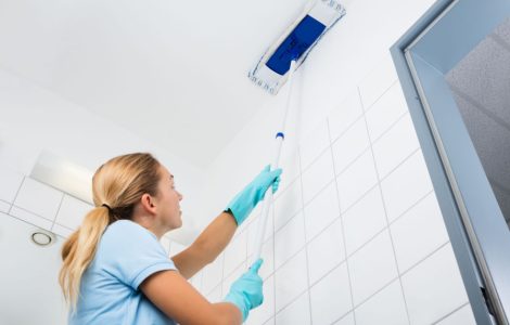 Une femme avec des gants bleus nettoie le plafond avec un mop