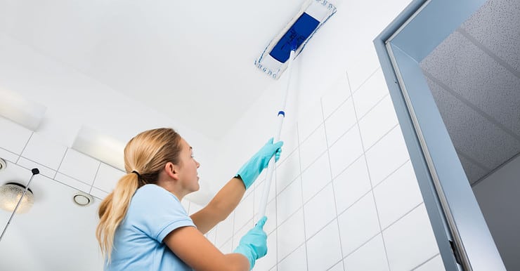 Une femme avec des gants bleus nettoie le plafond avec un mop