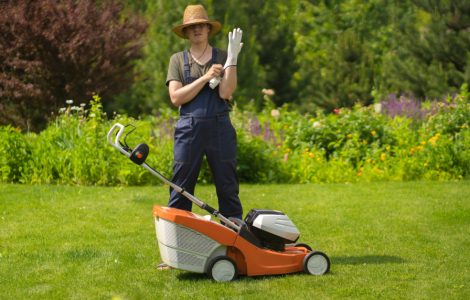 Une personne en chapeau se prépare à tondre la pelouse avec une tondeuse à gazon