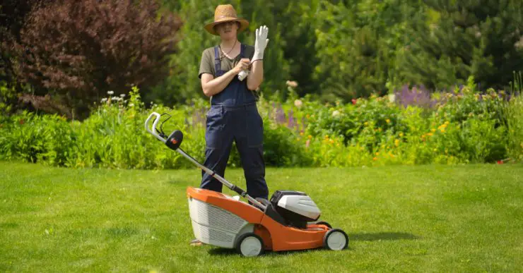 Une personne en chapeau se prépare à tondre la pelouse avec une tondeuse à gazon