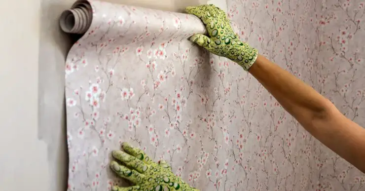 Zoom sur les mains d'une femme posant un rouleau de papier peint fleuri sur le mur