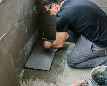 Un homme à lunette commence à carreler une terrasse