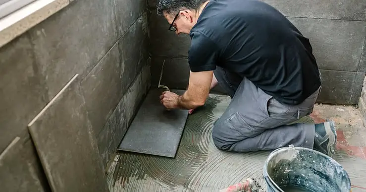 Un homme à lunette commence à carreler une terrasse