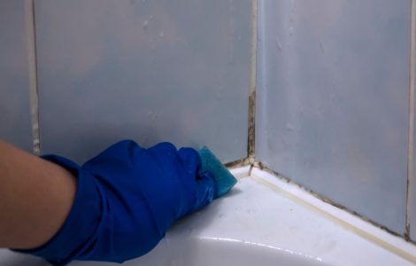 Une main en gant bleu nettoie le coin de la baignoire