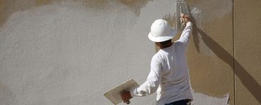 Un homme en casque blanc applique un enduit sur le mur extérieur d’un bâtiment