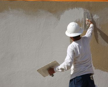 Un homme en casque blanc applique un enduit sur le mur extérieur d’un bâtiment