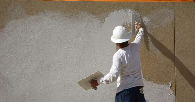 Un homme en casque blanc applique un enduit sur le mur extérieur d’un bâtiment