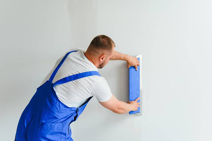 Un homme en salopette bleu en train de lisser un mur de plâtre