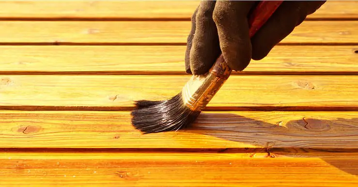 Main d'un homme appliquant du vernis sur un meuble en bois