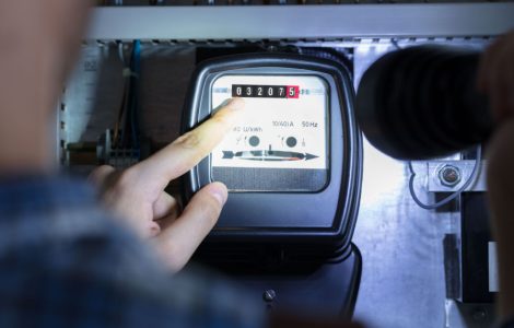 Un homme avec une lampe pointe son doigt sur un compteur électrique pour lire les chiffres
