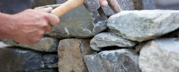 Un homme avec un marteau construit un muret en pierres sèches